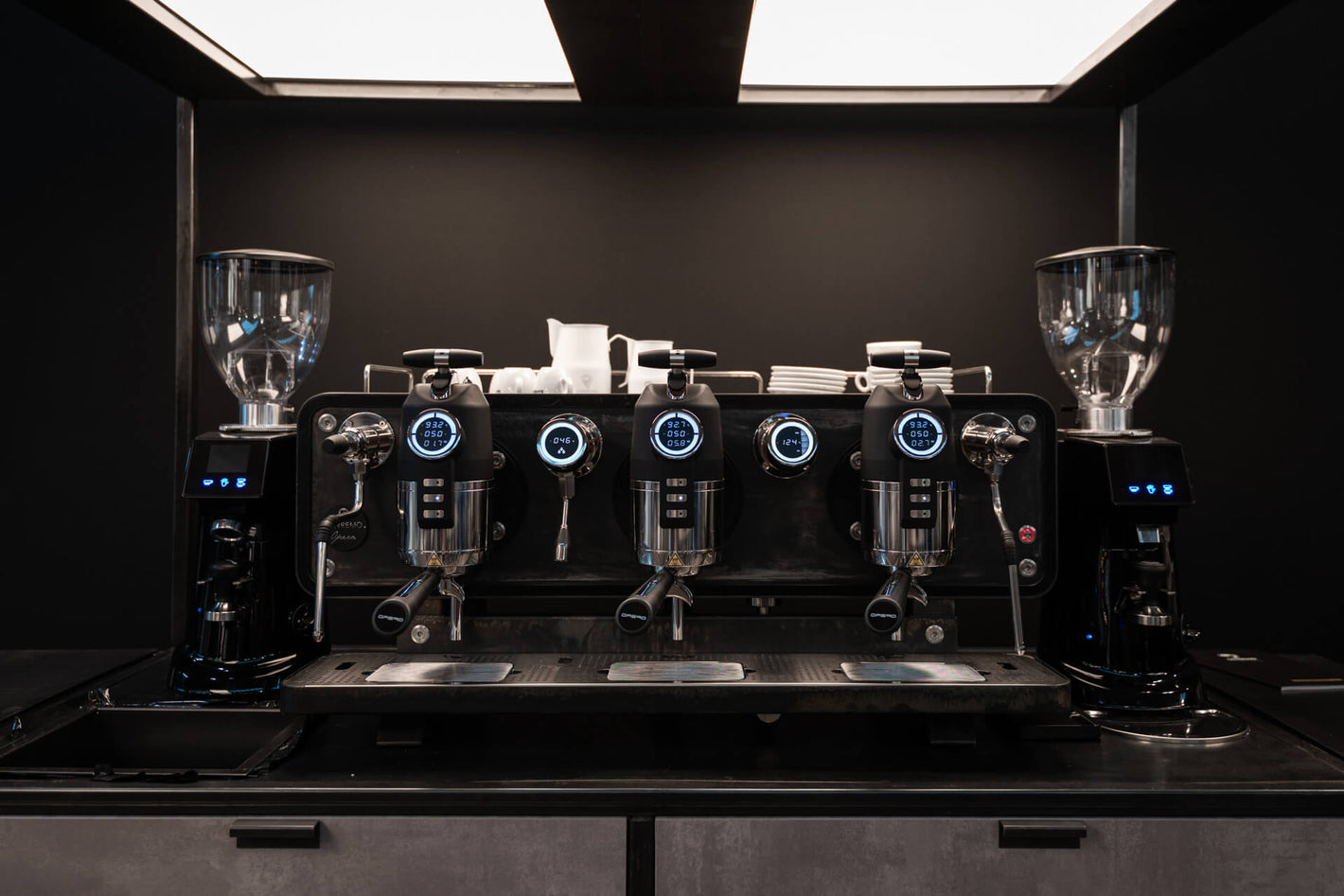 Sanremo Opera 3 groups professional espresso machine in black with two Sanremo coffee grinders, one at each side, all with illuminated displays, front view