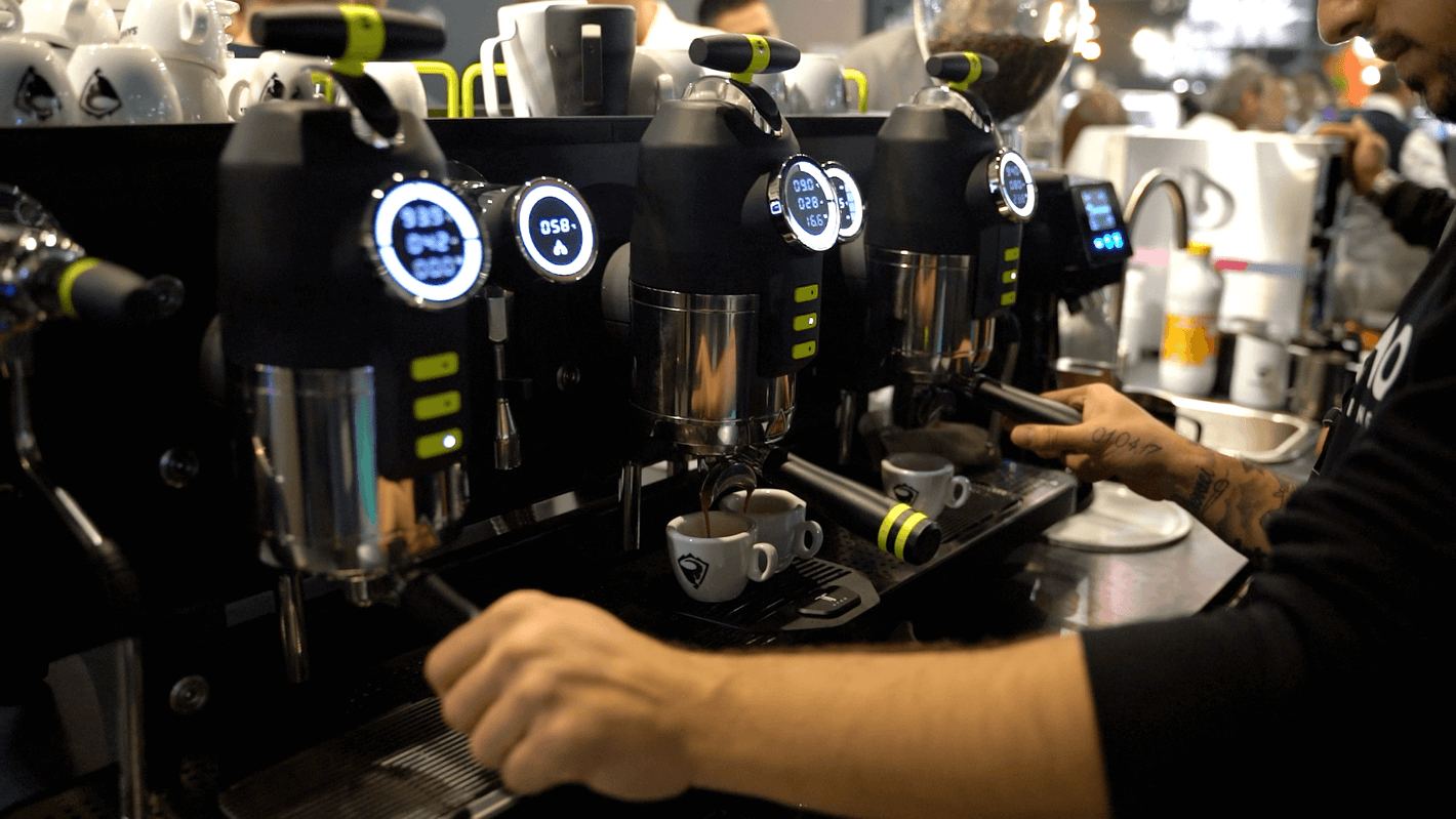 Barista pulling a shot on Sanremo Opera Espresso Machine during a demo session at a Sanremo booth at the coffee equipment expo with a crowd

